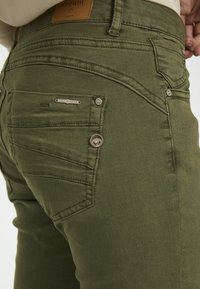 Olivgröna denimjeans med smal passform, utrustade med bakfickor, subtila sömdetaljer och metalliska detaljer. 