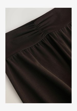 Tumepruun seelik, millel on kokku volditud vöökoht, valmistatud pehmest ja siledast kangast. Disain sisaldab voltide voolamist vöökoha alt allapoole.