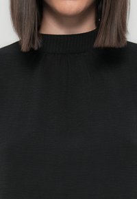 Black top with a ribbed neckline, featuring subtle pleats and a smooth texture, covering the upper chest and neck area.