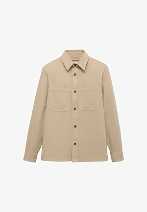 Beige skjorte med knaplukning og krave, to brystlommer, lange ærmer og sorte knapper. Lavet af bomuld med en glat tekstur.