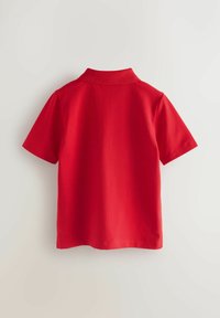 Polo rojo de manga corta con cuello. Hecho de una tela suave, tiene un corte simple y sin patrones o acentos visibles.