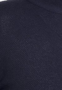 Marinblå stickad tyg med en strukturerad mönster, som har en något lös väv och en subtil lyster. Inga ytterligare detaljer eller accenter är synliga.