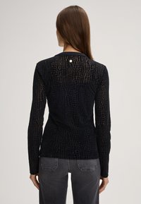 Maglietta nera a maniche lunghe con un motivo testurizzato a forma di rettile, caratterizzata da un collo rotondo e un piccolo accento circolare sul retro.