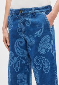 Μπλε τζιν παντελόνια με ανοιχτό μπλε σχέδιο πεϊσλεϊ, σχεδιασμένα με κούμπωμα με κουμπί και πλαϊνές τσέπες. Ορατή λεπτομέρεια υφής υφάσματος.