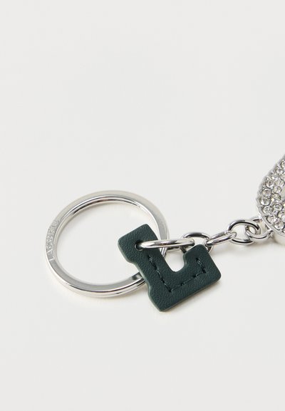 Porte-clés en métal argenté avec un pendentif en cuir vert foncé en forme de lettre « L » et un accessoire orné de strass fixé par une chaîne.