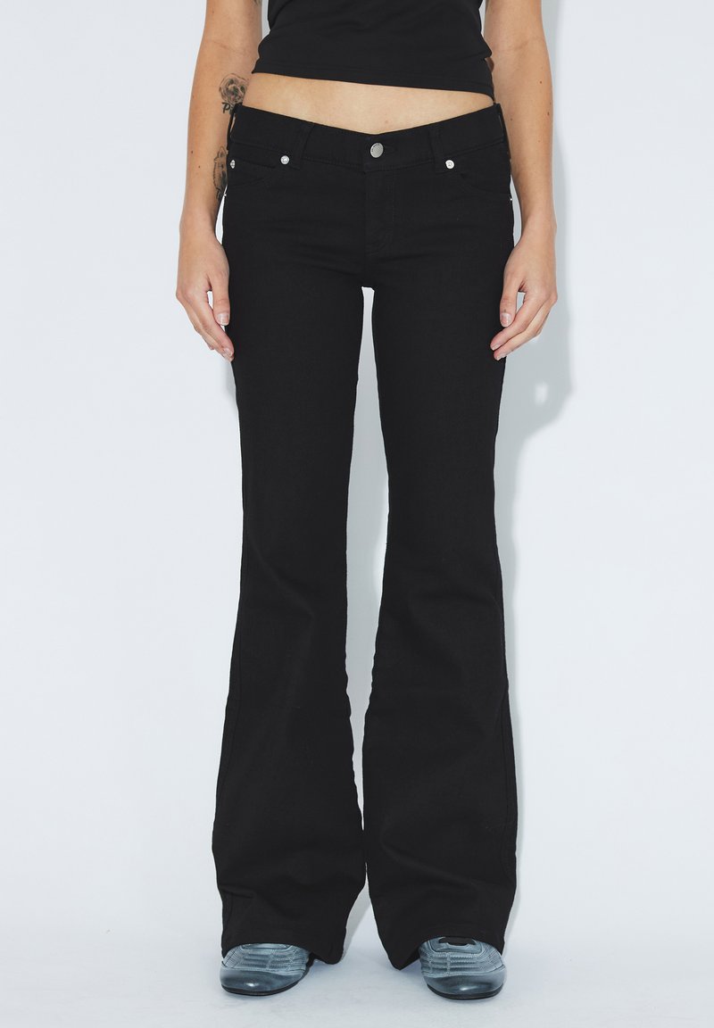Schwarze Schlagjeans aus Denim, mit einem klassischen fünf-Taschen-Design, silbernem Zubehör und einer taillierten Passform oberhalb der Schlagbeine.
