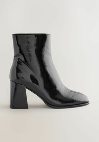 Black patent leather ankle boot with a square toe and wide block heel, featuring a smooth, reflective surface and minimalist design.