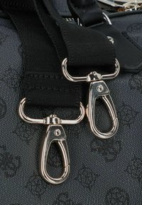 Sac en tissu noir avec un motif texturé, bandoulière noire réglable et fermetures en métal argenté pour une fermeture sécurisée.