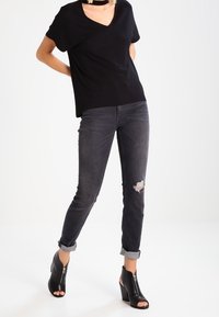Camisa negra de manga corta y escote en V combinada con jeans grises desgastados, con puños enrollados y botas de tacón abiertas negras con cremalleras.