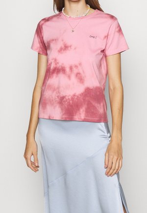 Femme portant un t-shirt tie-dye rose avec le texte « OMG ! » et une jupe en satin bleu clair, accessoirisée de colliers colorés en perles et pendentifs.