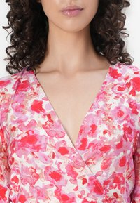 Abito a wrap floreale con motivi astratti in rosa, rosso e beige su tessuto leggero. Design a scollo a V e maniche leggermente drappeggiate.