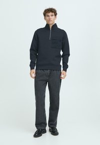 Navy blue fleece pullover with a high collar, half-zip, and a chest pocket. Paired with dark gray jeans and black shoes.