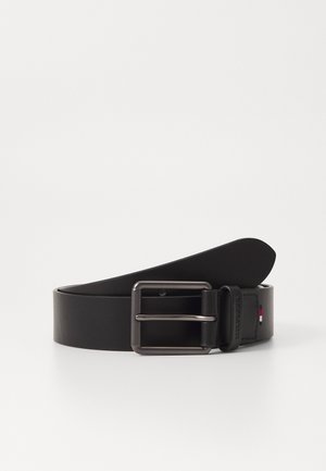 Ceinture en cuir noir avec une boucle en métal mat, dotée d'un design étroit et d'une extrémité surpiquée. Inclut un petit accent de logo en rouge, blanc et bleu.