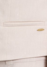 Helles rosa Anzuggewebe mit einem subtilen diagonalen Streifenmuster. Verfügt über eine aufgesetzte Tasche und einen goldenen Hardware-Akzent mit dem Markennamen.