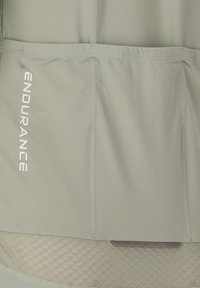 Vaaleanvihreä kangas, jossa ommellut saumat ja vasemmalla puolella valkoinen pystysuora "ENDURANCE"-teksti, teksturoidun verkkokankaan yläpuolella.