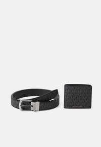 Cintura nera Michael Kors con fibbia argento e portafoglio nero abbinato con motivo a logo MK ripetuto, esposti su sfondo bianco.