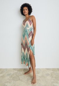 Long dress featuring zigzag patterns in turquoise, peach, and brown, with a front slit and thin spaghetti straps, made from lightweight fabric.