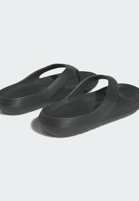 Svarta plastsandaler med en flexibel rem, strukturerad yta och dämpad sula. Har en lätt svank och ribbad detaljering på sidorna.