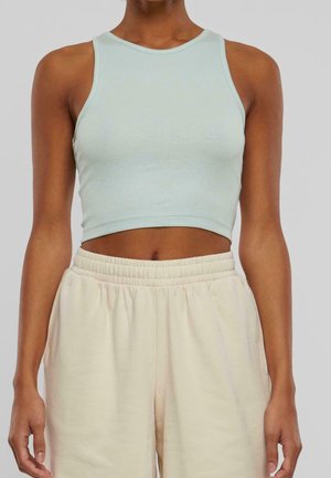Woman wearing a light blue sleeveless crop top and high-waisted beige drawstring pants against a plain background.