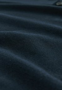 Tumedat sinised kangad pehme, tekstureeritud pinnaga, millel on detailirohked voldid ja sujuvad, kudumise mustrid.