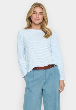 Cămașă cu mânecă lungă, cu dungi în albastru deschis și alb, cu o croială lejeră. Asortată cu pantaloni din denim deschis cu talie înaltă și picioare largi, purtați cu o curea maro.