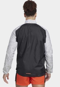 Lekka kurtka z czarnym korpusem i szarymi, paskowanymi rękawami. Materiał jest gładki z delikatnym połyskiem, zaprojektowany do aktywnego noszenia.