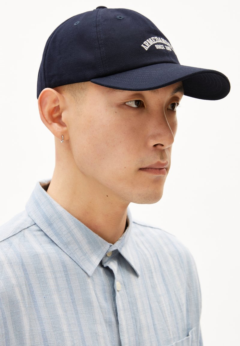 Marineblauwe baseballpet met geborduurd logo aan de voorkant, voorzien van een gebogen klep en stoffen oogjes voor ventilatie.