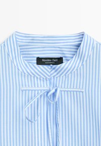 Chemise à rayures verticales bleu clair et blanches avec un col rond et un détail de nouage à l'avant, étiquetée "Massimo Dutti, Fabriqué au Portugal."