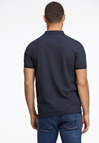 Laivastonsininen poolopaita, jossa on kaulus ja lyhyet hihat, teksturoitua kangasta ja suora helma, yhdistettynä sinisiin farkkuihin.