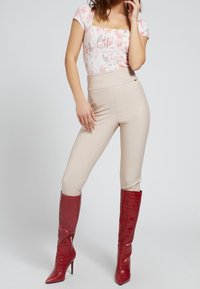 Tætsiddende beige leggings kombineret med en bluse med blomsterprint. Modellen har røde, højhælede støvler lavet i krokodillepræget læder på.