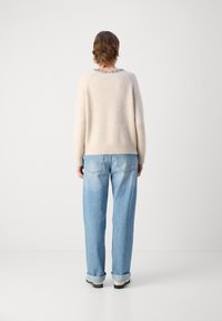 Pull en tricot beige avec un col rond et des bords texturés, associé à un jean ample bleu clair, avec des poignets retroussés et des poches arrière.