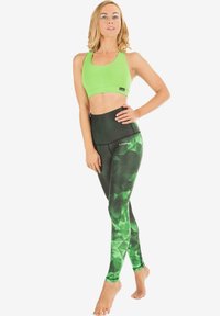 Grüner Sport-BH und hochtaillierte Leggings mit einem geometrischen grünen Muster. Beide Teile verfügen über eine glatte Textur und eine enge Passform.