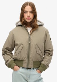 Khaki bomberjack met een grijze capuchon, ritssluiting en twee voorzakken. Ribgebreide manchetten en zoom, gemaakt van lichtgewicht stof.