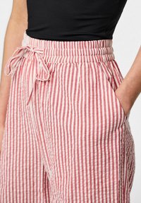 Růžové a bílé pruhované lněné kalhoty s elastickým pasem a detaily na zavazování. Obsahují boční kapsy a volný střih.