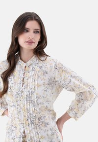 Floral blouse with long sleeves, featuring yellow and gray flower patterns on a white background, pleated design, and button closure.