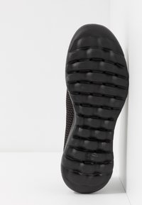 Scarpa sportiva nera con una parte superiore testurizzata e una suola in gomma flessibile e rigata, con punta arrotondata e dettagli in rete sul lato.
