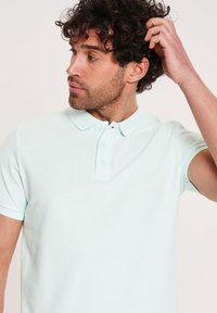 Lys mintgrøn kortærmet polo skjorte lavet af struktureret stof, med en tre-knaps placket og et lille logo på brystet.