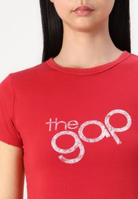 Rode katoenen t-shirt met een ronde halslijn en korte mouwen. Heeft een opvallend wit glinsterend logo met de tekst "the gap" op de borst.