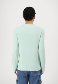 Un pull vert menthe avec un tricot texturé, des manches longues et un col rond, associé à un pantalon cargo bleu avec des poches.
