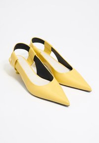 Gelbe Slingback-Schuhe mit spitzem Zehenbereich, glänzender Oberfläche und schwarzen Akzenten. Sie verfügen über einen niedrigen Absatz und ein ausgeschnittenes Seitendesign.