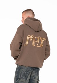 Brauner Kapuzenpullover mit großer goldfarbener, seil-texturierter "MPLY" Stickerei auf dem Rücken. Verfügt über eine überschnittene Passform und weichen Stoff.