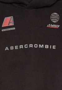 Musta huppari, jossa on harmaa "ABERCROMBIE" -teksti, logopatchit ja maapallon grafiikka. Omistaa pehmeän tekstuurin ja normaali istuvuus.