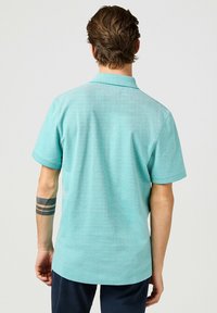 Polo shirt turchese chiaro con maniche corte, colletto e una texture liscia. Presenta un orlo dritto e cuciture rinforzate.