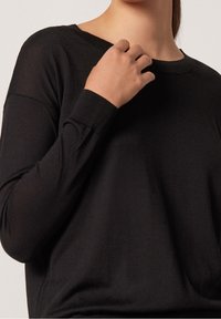 Haut noir à manches longues avec une coupe décontractée, fabriqué dans un matériau doux, présentant un col et des poignets côtelés, avec une texture lisse.