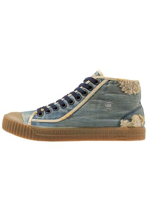 Baskets montantes en denim bleu, finition beige, lacets bleu marine, semelle en gomme et zones usées au talon et sur le côté supérieur.