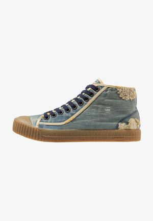 High-top sneaker met blauw denimstof, beige afwerking, navy veters, rubberen zool en versleten plekken op de hiel en bovenkant.