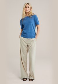 Zils adīts īsām piedurknēm džemperis ar paceltu tekstūru, kombinēts ar gaiši beigu plaša kāju biksēm un melniem atvērtu pirkstu apaviem.