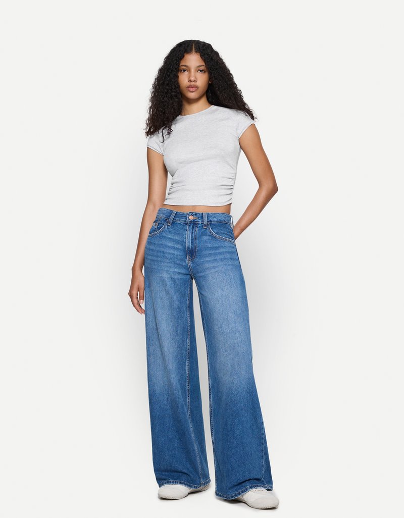 Light gray fitted t-shirt paired with wide-leg blue jeans. Jeans feature a high waist, denim texture, and subtle stitching details.