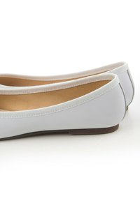 Ballerines grises avec une finition lisse et mate, un bord élastique et une semelle brune plate, dotées d'un design à bout ovale.
