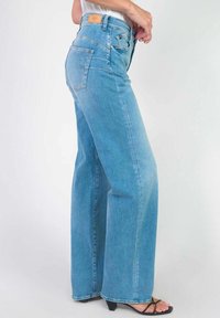 Jeans taille haute bleu clair en denim, avec une coupe droite. Comprend deux poches arrière et une petite étiquette en cuir de la marque.